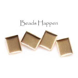 May include: Four gold-colored rectangular bezel trays are displayed on a white background. The trays are empty and ready for use. The text "Beads Happen" is written above the trays.