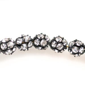 May include: A strand of oval-shaped beads with a black metal frame and clear rhinestones.