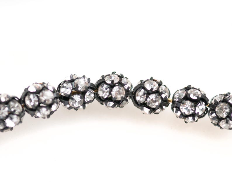 May include: A strand of oval-shaped beads with a black metal frame and clear rhinestones.