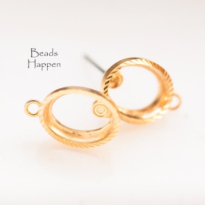 Puede incluir: Hallazgos de pendientes de metal dorado con un diseño circular. Los hallazgos tienen una superficie texturizada y un pequeño bucle en un lado. Los hallazgos están diseñados para sujetar una cuenta u otro adorno.