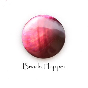 May include: A round, iridescent bead with a gradient of colors from pink to dark red. The surface has a swirling pattern. The text "Beads Happen" is written in black script below the bead.
