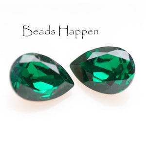 May include: Two pear-shaped emerald green glass beads. The beads are faceted and have a high shine.