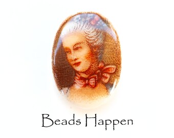 May include: Oval-shaped porcelain bead featuring a painted image of a woman with a white powdered wig and a pink ribbon. The bead has a brown background and a white border.