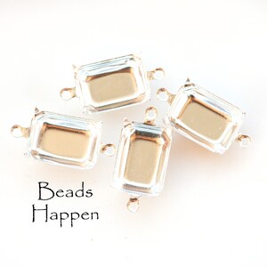 May include: Four clear glass rectangular bead caps with silver metal loops on each side. The bead caps are arranged in a pile on a white surface. The text "Beads Happen" is printed below the bead caps.