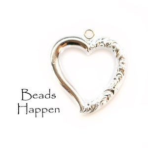 May include: Silver heart-shaped pendant with an ornate design. The pendant has a loop at the top for attaching to a chain or cord. The text "Beads Happen" is printed below the pendant.