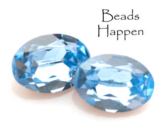 May include: Two oval-shaped, light blue gemstone beads. The beads are faceted and have a shiny, reflective surface. The text "Beads Happen" is visible in the background.
