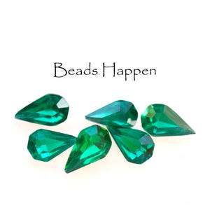 May include: Six emerald green teardrop-shaped glass beads. The beads are faceted and have a shiny finish. The beads are arranged in a cluster on a white background. The text "Beads Happen" is written in black above the beads.