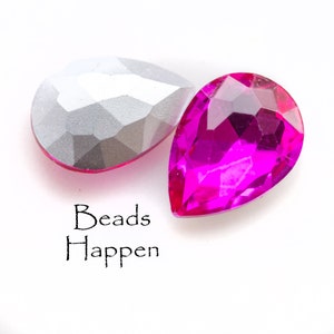 Puede incluir: Dos cuentas en forma de l&aacute;grima, una plateada y otra rosa brillante. Las cuentas son facetadas y tienen un acabado brillante. El texto "Beads Happen" est&aacute; impreso debajo de las cuentas.