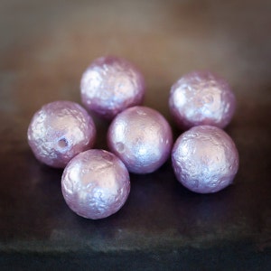 May include: Six iridescent pink pearl-like beads with a textured surface.