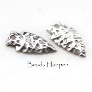 Könnte beinhalten: Zwei silberne Pfeilspitzen-Anhänger mit einer strukturierten Oberfläche. Die Pfeilspitzen haben oben ein Loch zum Anbringen an Schmuck.