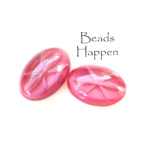 Puede incluir: Dos cuentas ovaladas de color rosa con un patrón de estrella. El texto "Beads Happen" está escrito encima de las cuentas.