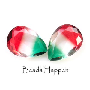 May include: Two teardrop-shaped glass beads with a red, white, and green ombre effect. The beads are faceted and have a glossy finish.