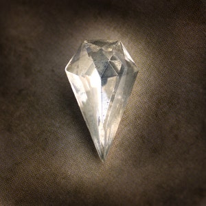 May include: A clear, faceted diamond-shaped object with a pointed base. The object is made of a transparent material, reflecting light and creating multiple internal facets. The background is a textured, dark brown fabric.