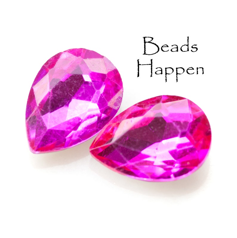 Puede incluir: Dos cuentas de color rosa nacarado en forma de l&aacute;grima sobre un fondo blanco. El texto "Beads Happen" est&aacute; escrito encima de las cuentas.