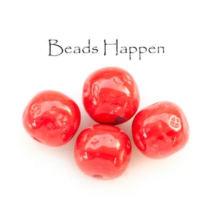 May include: Four bright red round beads, with a glossy finish, on a white background. The text "Beads Happen" is written above the beads.
