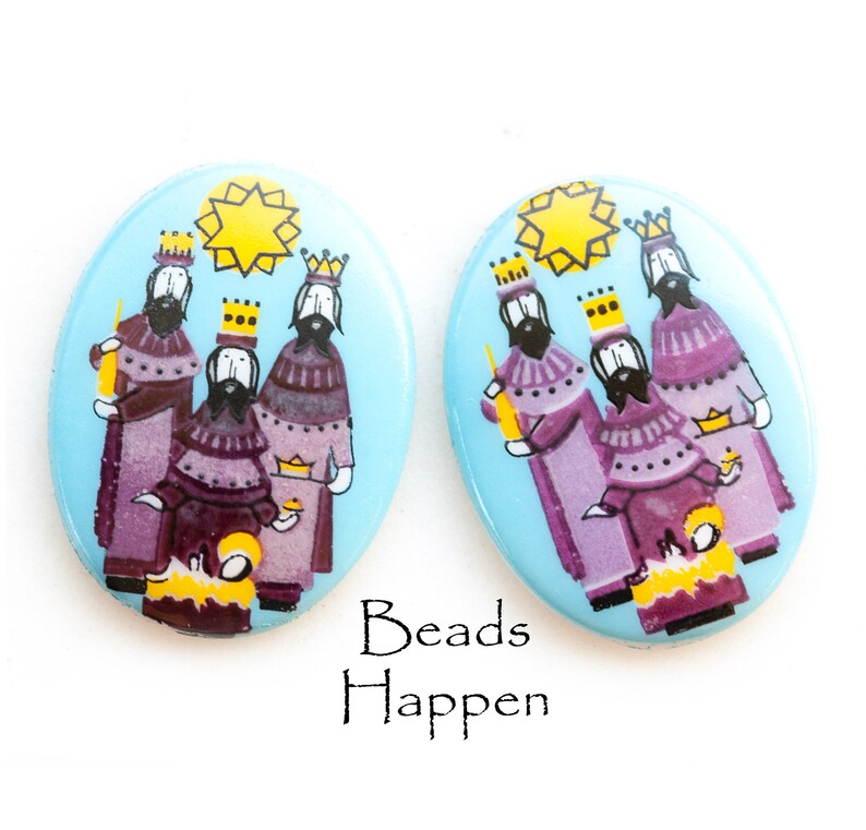 May include: Pair of oval-shaped ceramic earrings with a blue background and a depiction of the three wise men in purple robes, carrying gifts and following a yellow star.