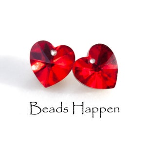 Op de afbeelding: Twee rode hartvormige kristallen kralen met een gat in het midden. De kralen liggen op een witte achtergrond. Beads Happen.
