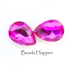 Puede incluir: Dos cuentas de vidrio de forma de l&aacute;grima, de color rosa nacarado. Las cuentas son facetadas y tienen un acabado brillante. Beads Happen est&aacute; escrito debajo de las cuentas.