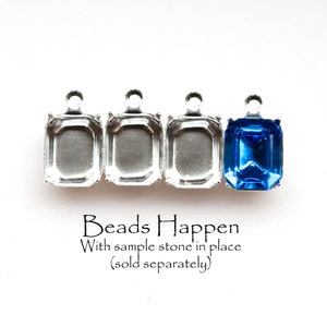 Puede incluir: Cuatro engastes metálicos plateados para engastes de bisel, con un engaste lleno de una piedra preciosa azul. El texto "Beads Happen" está debajo de los engastes, con el texto "With sample stone in place (sold separately)" debajo de ese.