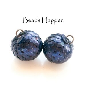 May include: Two dark blue round beads with a scaly texture. The beads have a silver loop at the top. The text "Beads Happen" is written above the beads.