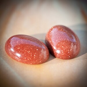 Puede incluir: Dos piedras ovaladas de color rojo pulidas con una textura brillante y moteada.
