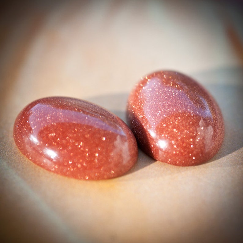 Puede incluir: Dos piedras ovaladas de color rojo pulidas con una textura brillante y moteada.