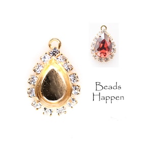 May include: Gold teardrop pendant with a clear crystal halo and a blank center for adding a cabochon. The pendant is shown with a red cabochon in the center.
