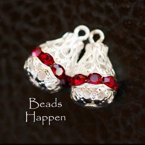 May include: Two silver filigree bead caps with red rhinestone accents. The caps are designed to be used for jewelry making.