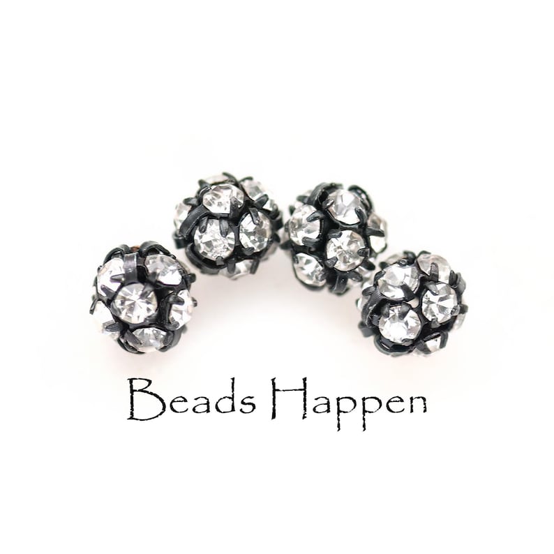 May include: Four black and silver round beads with rhinestones. The beads are arranged in a semi-circle. The text "Beads Happen" is below the beads.