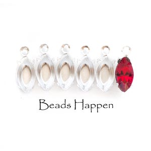 May include: Six silver-colored marquise-shaped jewelry findings, one with a vibrant red gemstone. The findings have a loop at the top for attaching to other components. The text "Beads Happen" is printed below the findings.