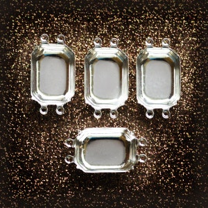 May include: Four silver-toned metal frames with a beveled edge and three loops on each side. The frames are arranged in a row with the bottom frame slightly offset.