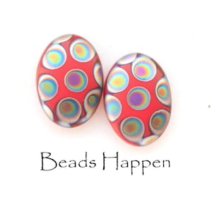 May include: Two red oval-shaped beads with iridescent circles on a white background. The beads have a speckled look and are made of glass. The text "Beads Happen" is printed below the beads.