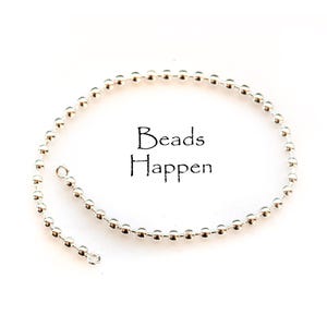 May include: A silver-colored ball chain with a loop at one end, and the text "Beads Happen" in black script. The chain is composed of small, evenly spaced, spherical beads. The background is plain white.