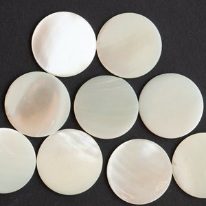 May include: Nine white, round, mother-of-pearl buttons arranged in a pyramid shape on a black background.