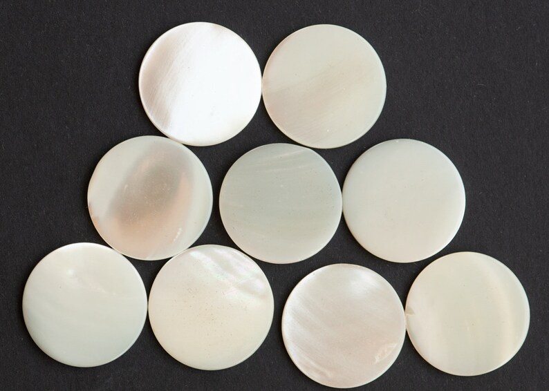 May include: Nine white, round, mother-of-pearl buttons arranged in a pyramid shape on a black background.