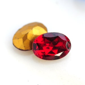 May include: Two oval-shaped rhinestones, one gold and one red. The red rhinestone is faceted and has a starburst pattern.
