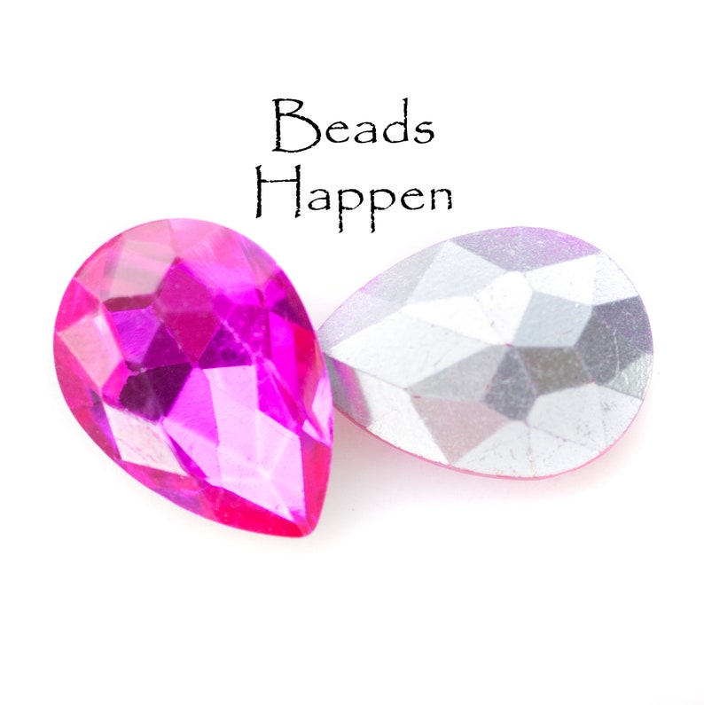 Puede incluir: Dos cuentas de vidrio en forma de l&aacute;grima, una rosa y otra plateada, con el texto "Beads Happen" encima.