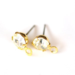 May include: A pair of gold-tone earring findings with clear rhinestone accents. The findings have a small loop on the side for attaching a charm or pendant.
