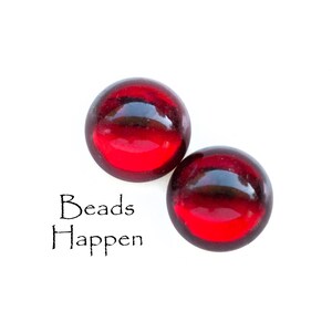 May include: Two red glass beads on a white background. The text "Beads Happen" is written below the beads.
