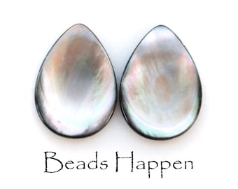 May include: Two iridescent black teardrop-shaped shell beads. The beads have a pearlescent sheen and are smooth and polished.