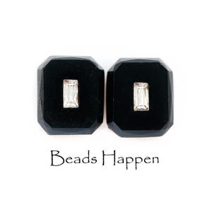 May include: Two black square-shaped beads with a clear rectangular stone set in the center of each bead. The beads are on a white background. Beads Happen is written below the beads.