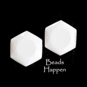 May include: Two white hexagonal ceramic beads. The beads are smooth and glossy. The text "Beads Happen" is visible below the beads.