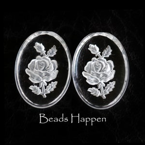 May include: Two clear glass oval-shaped beads with a carved rose design. The roses are detailed with leaves and stems.