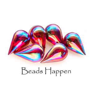 May include: A group of six iridescent teardrop-shaped glass beads in shades of red, pink, and orange. The beads have a glossy finish and are arranged in a cluster on a white background. The text "Beads Happen" is printed below the beads.