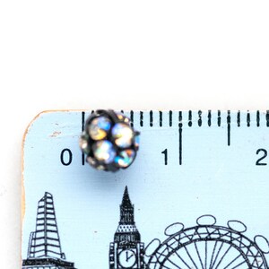 May include: A blue wooden ruler with black markings and a black and iridescent rhinestone embellishment. The ruler has the numbers 0, 1, and 2 printed on it. The ruler has a design of London landmarks printed on it, including Big Ben and the London Eye.