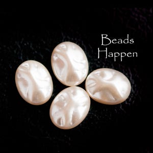 Puede incluir: Cuatro cuentas ovaladas de color blanquecino con un brillo nacarado. Las cuentas tienen una superficie ligeramente irregular y están dispuestas sobre un fondo negro. El texto "Beads Happen" está en escritura blanca.