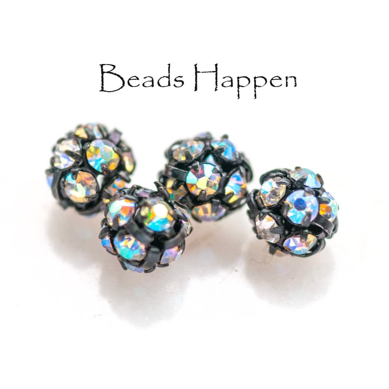 May include: Four iridescent black and silver round beads with a faceted design.  The beads are about 1/2 inch in diameter.  The beads are on a white surface.  "Beads Happen" is written in black text above the beads.