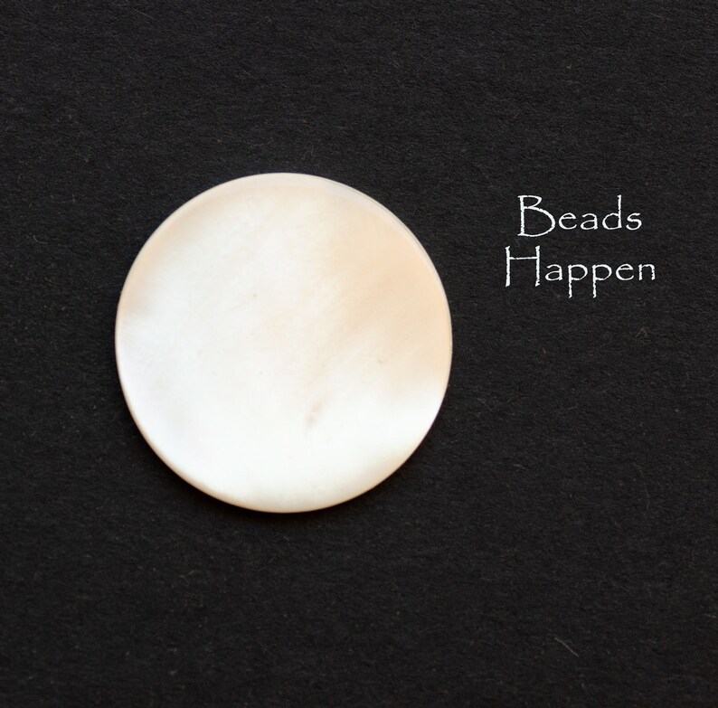May include: A white, round, smooth, and shiny bead. The bead is on a black background. The text "Beads Happen" is written in white on the right side of the image.