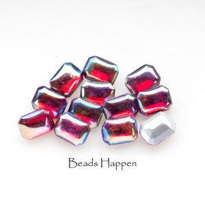May include: A group of 11 iridescent red and purple glass beads, with one silver bead. The beads are shaped like rectangles with rounded corners. The beads are arranged in a pile on a white surface. The text "Beads Happen" is printed below the beads.