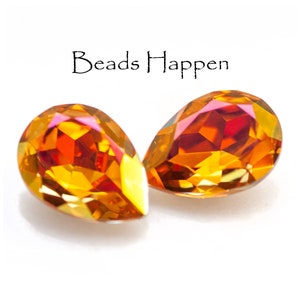 Puede incluir: Dos cuentas de vidrio iridiscente de color naranja y rojo en forma de lágrima. Las cuentas tienen un diseño facetado y están sobre un fondo blanco.